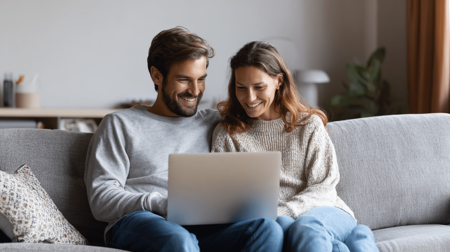 A young couple in their living room searching for a home to purchase on their laptop.